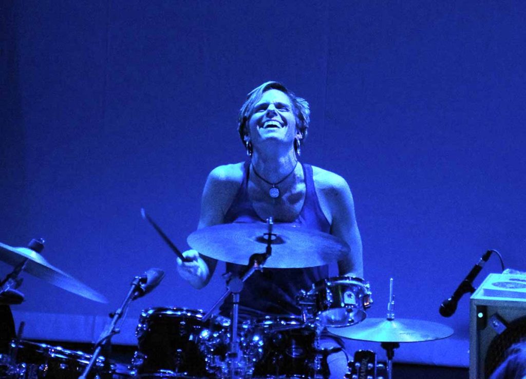 JJ Clarke playing drums on stage under blue lights