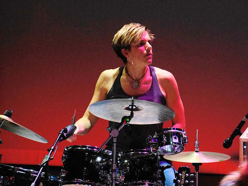 JJ Clarke playing drum kit with red background